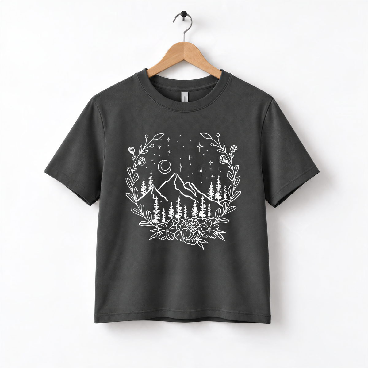 A black t-shirt with a white graphic design depicting a mountain landscape with a wreath of flowers and stars above it.
