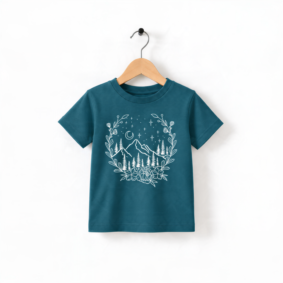A teal-colored t-shirt with a white floral design and mountain landscape printed on it, hanging on a wooden hanger.