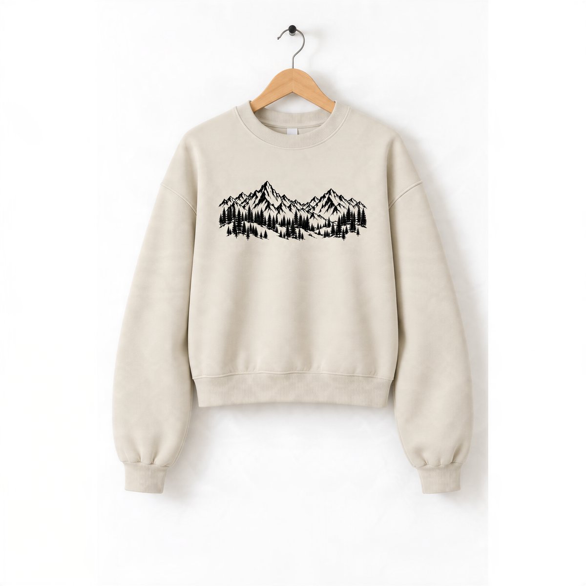 A beige sweatshirt with a graphic design of mountains and trees printed on it, hanging on a wooden hanger.