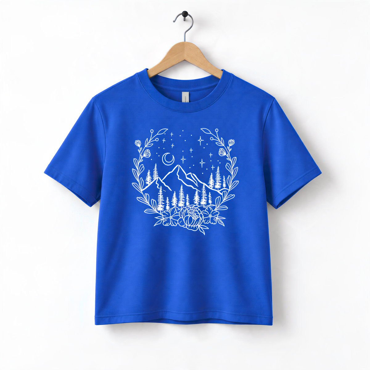 A blue t-shirt with a white graphic design depicting a mountain landscape with trees, flowers, and stars.