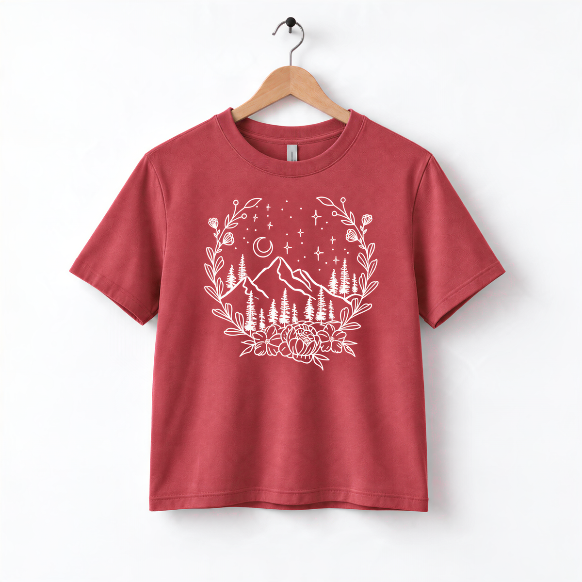 A red t-shirt with a white graphic design depicting a mountain landscape with trees, flowers, and stars.