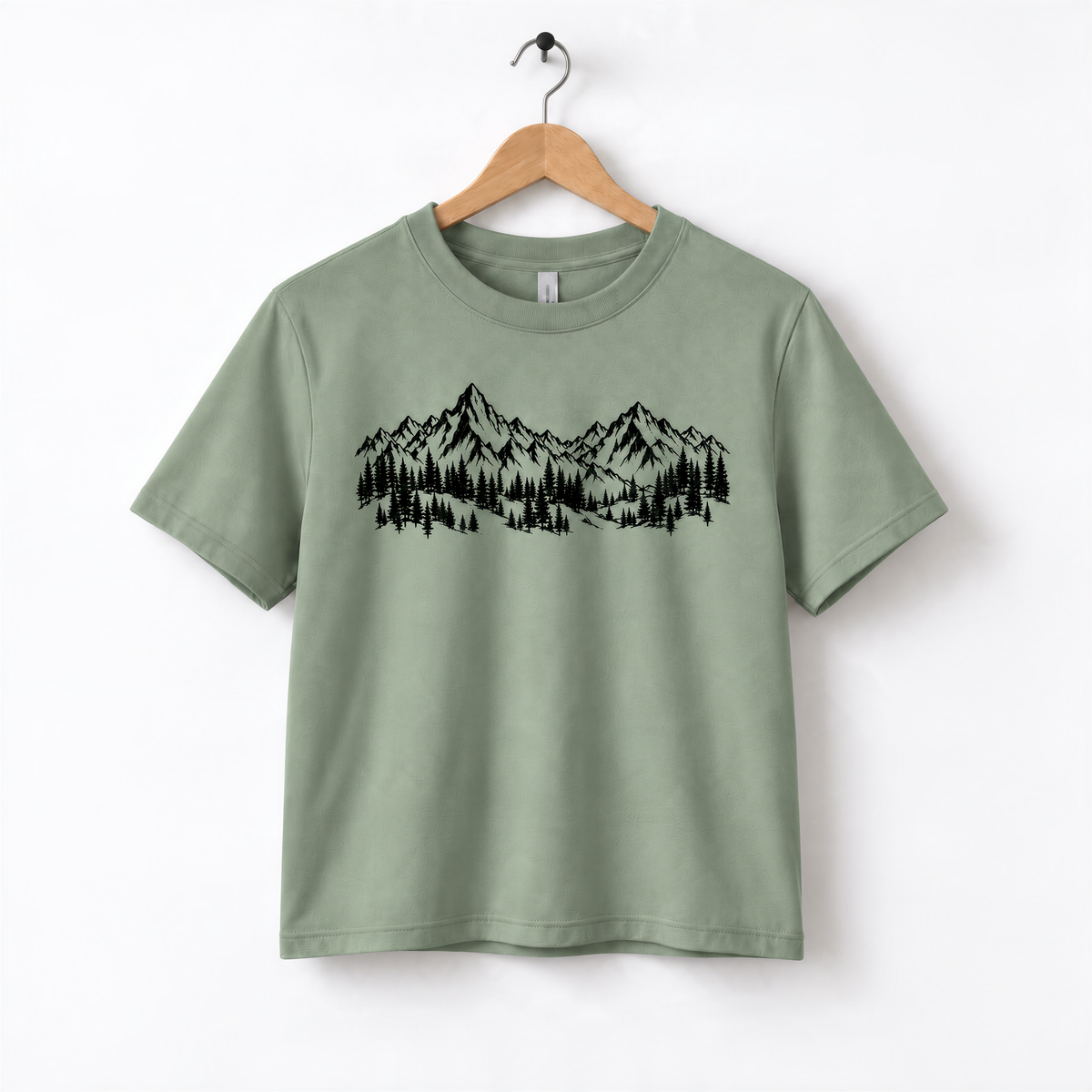 A green t-shirt with a graphic design of mountains and trees printed on it, hanging on a wooden hanger.