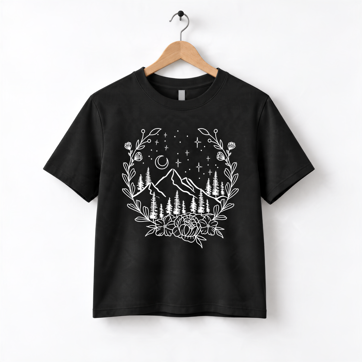A black t-shirt with a white graphic design depicting a mountain landscape with trees, flowers, and stars in the night sky.