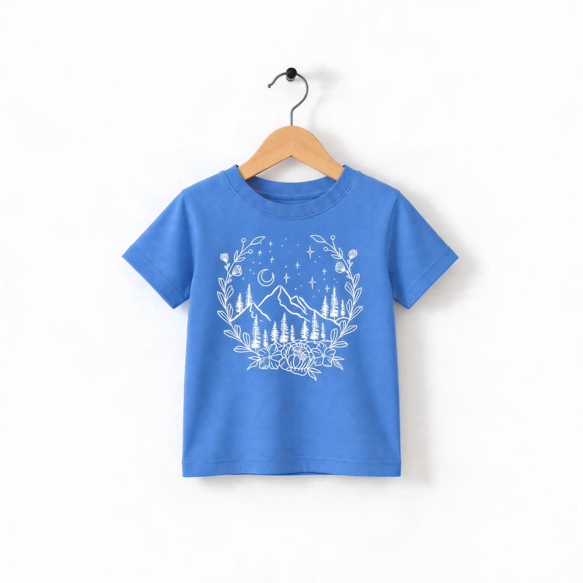 A blue t-shirt with a white graphic design depicting a mountain landscape with trees, flowers, and stars.