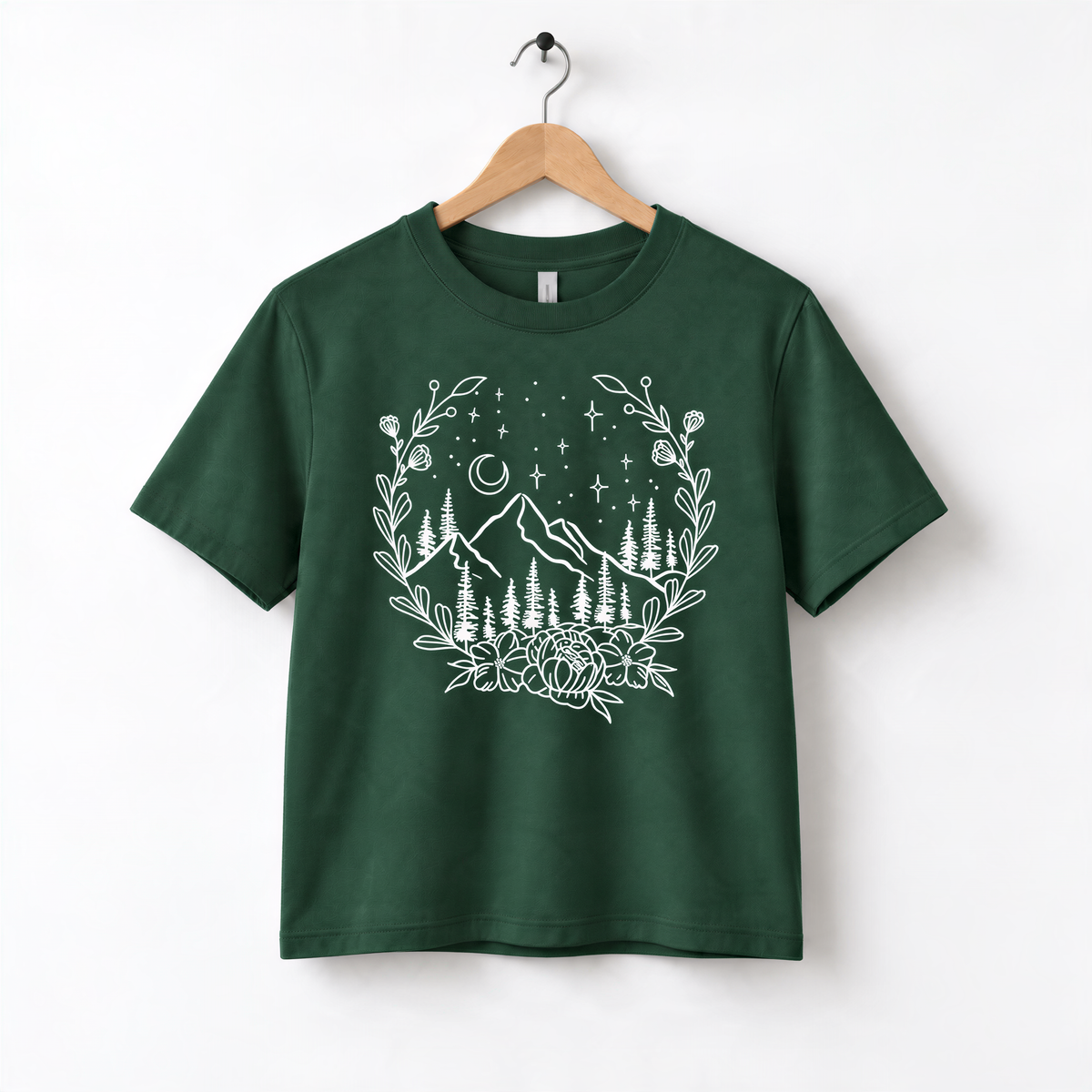 A green t-shirt with a white graphic design depicting a mountain landscape with trees, flowers, and a crescent moon.