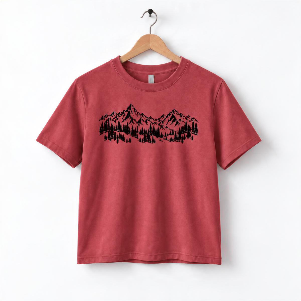 A red t-shirt with a graphic design of mountains and trees printed on it, hanging on a wooden hanger.