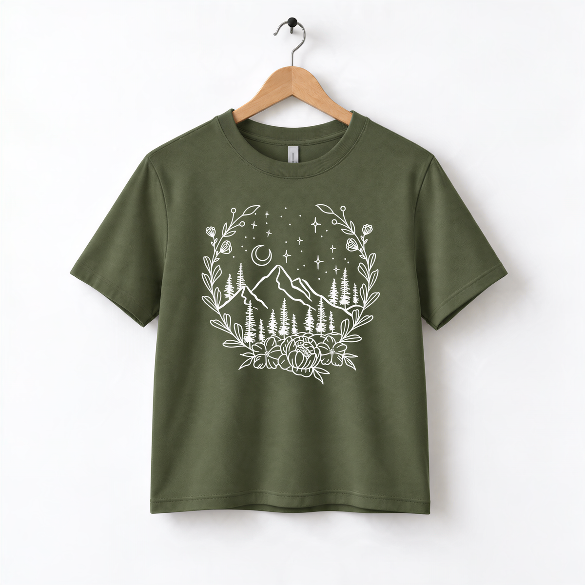 A green t-shirt with a white graphic design depicting a mountain landscape with trees, flowers, and stars in the night sky.
