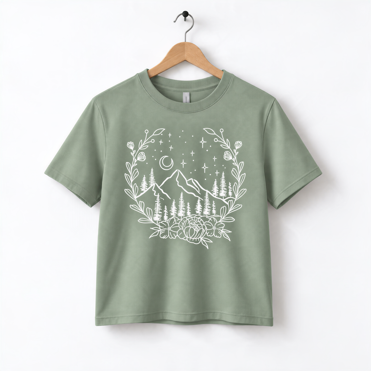 A green t-shirt with a white graphic design depicting a mountain landscape with trees, flowers, and stars.