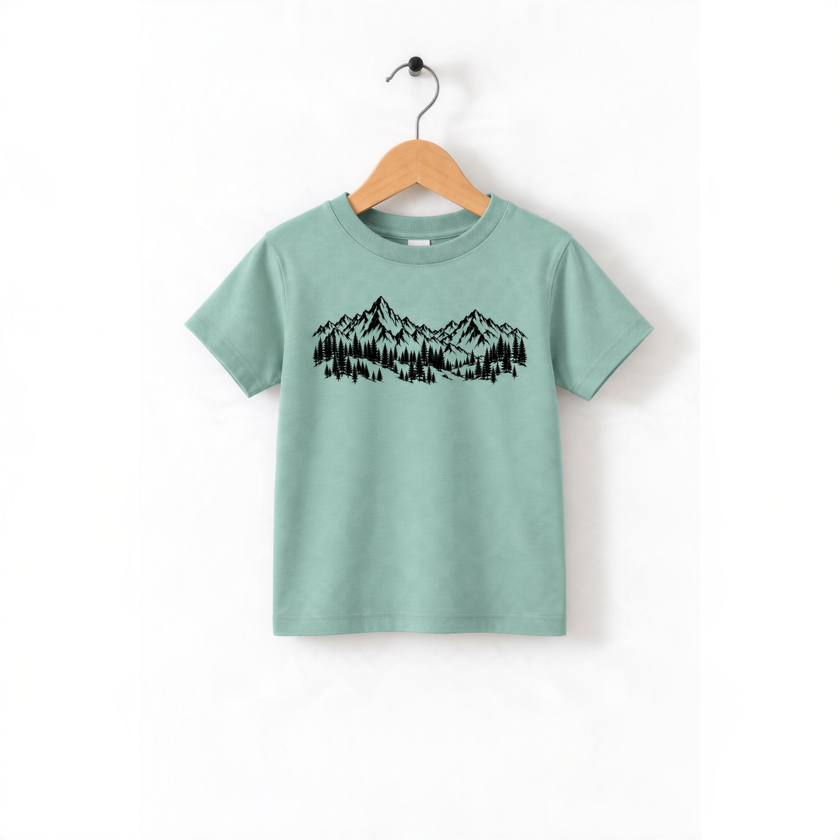 A light green t-shirt with a graphic design of mountains and trees printed on it, hanging on a wooden hanger.