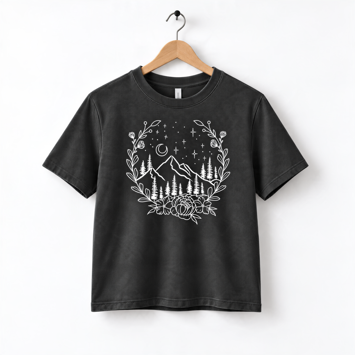 A black t-shirt with a white graphic design depicting a mountain landscape with trees, flowers, and stars.