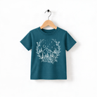 A teal-colored t-shirt with a white floral design and mountain landscape printed on it, hanging on a wooden hanger.