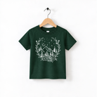 A green t-shirt with a white graphic design depicting a mountain landscape with trees, flowers, and stars.