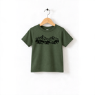 A green t-shirt with a graphic design of mountains and trees printed on it, hanging on a wooden hanger.