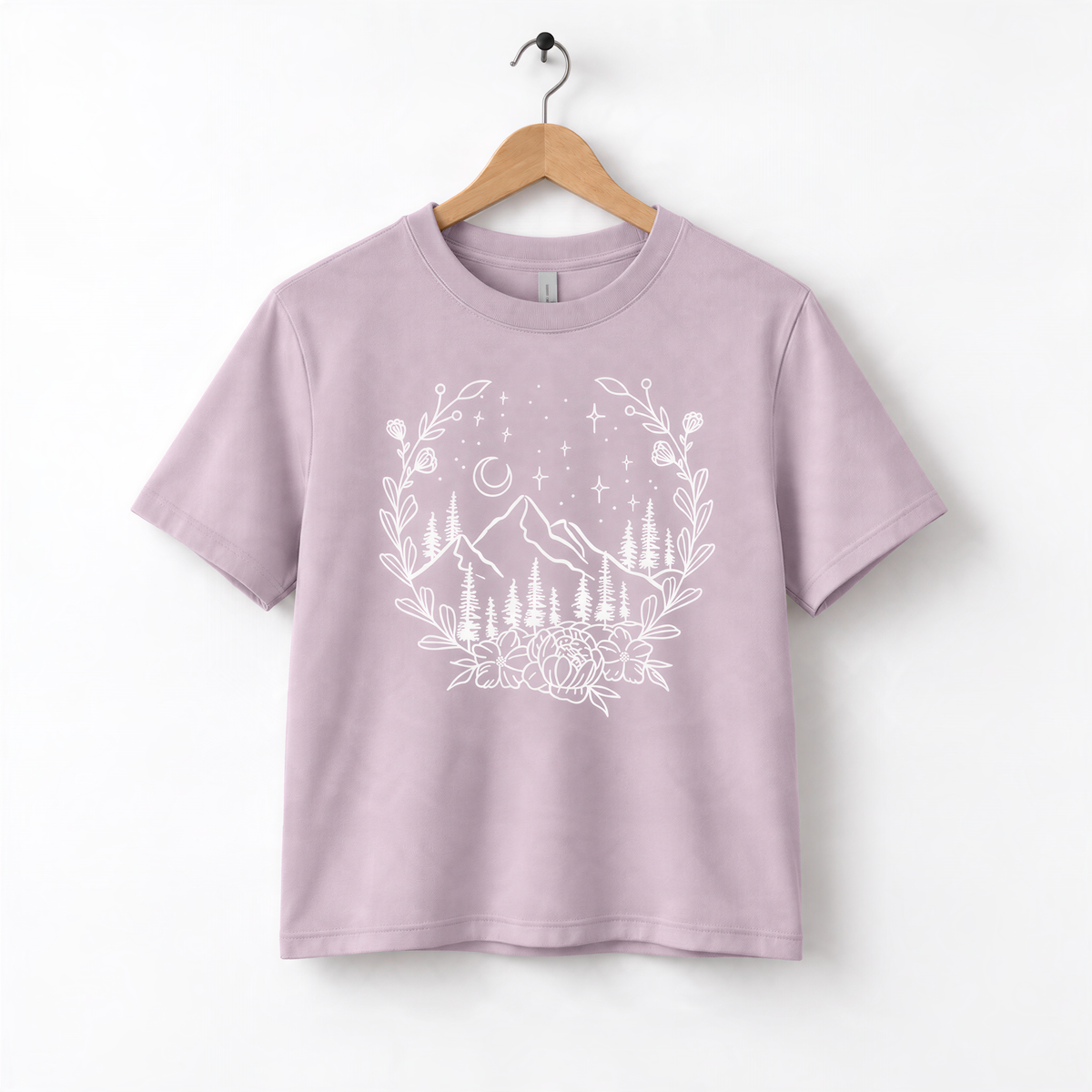 A light purple t-shirt with a white graphic design depicting a mountain landscape with trees, flowers, and stars.