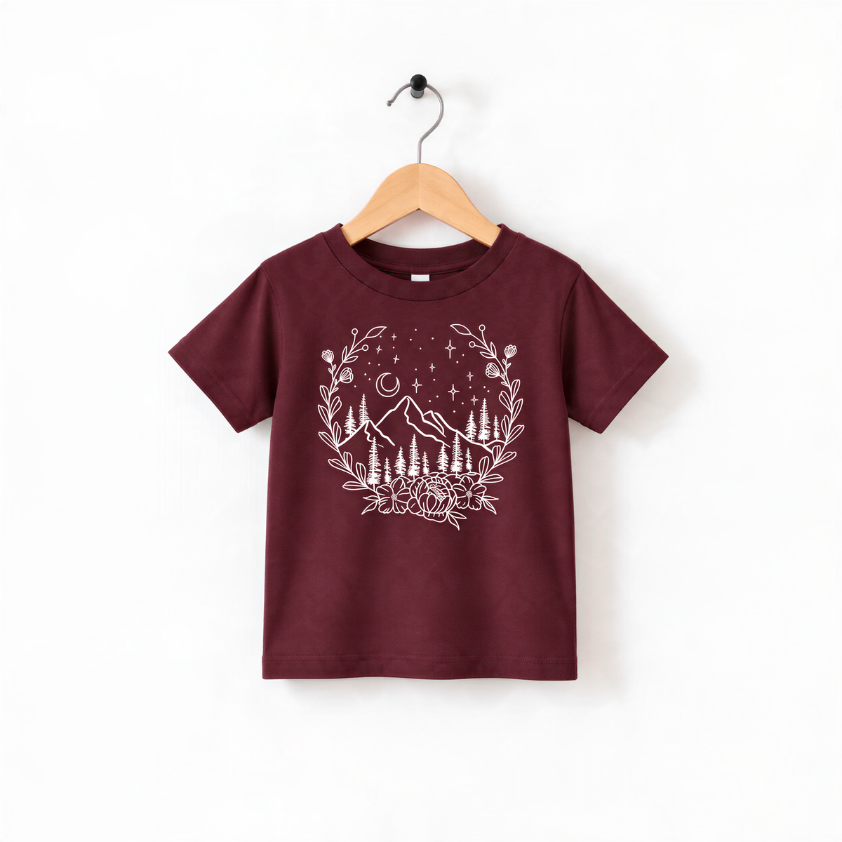 A burgundy-colored t-shirt with a white graphic design depicting a mountain landscape with trees, mountains, and stars.