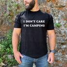 Man wearing a black t-shirt with 'I DON'T CARE I'M CAMPING' text, standing against a natural background.