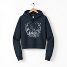 A navy blue hoodie with a white graphic design depicting a mountain landscape with trees, flowers, and stars on a dark background.