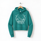 A teal hoodie with a white floral design on the front, hanging on a wooden hanger against a white background.