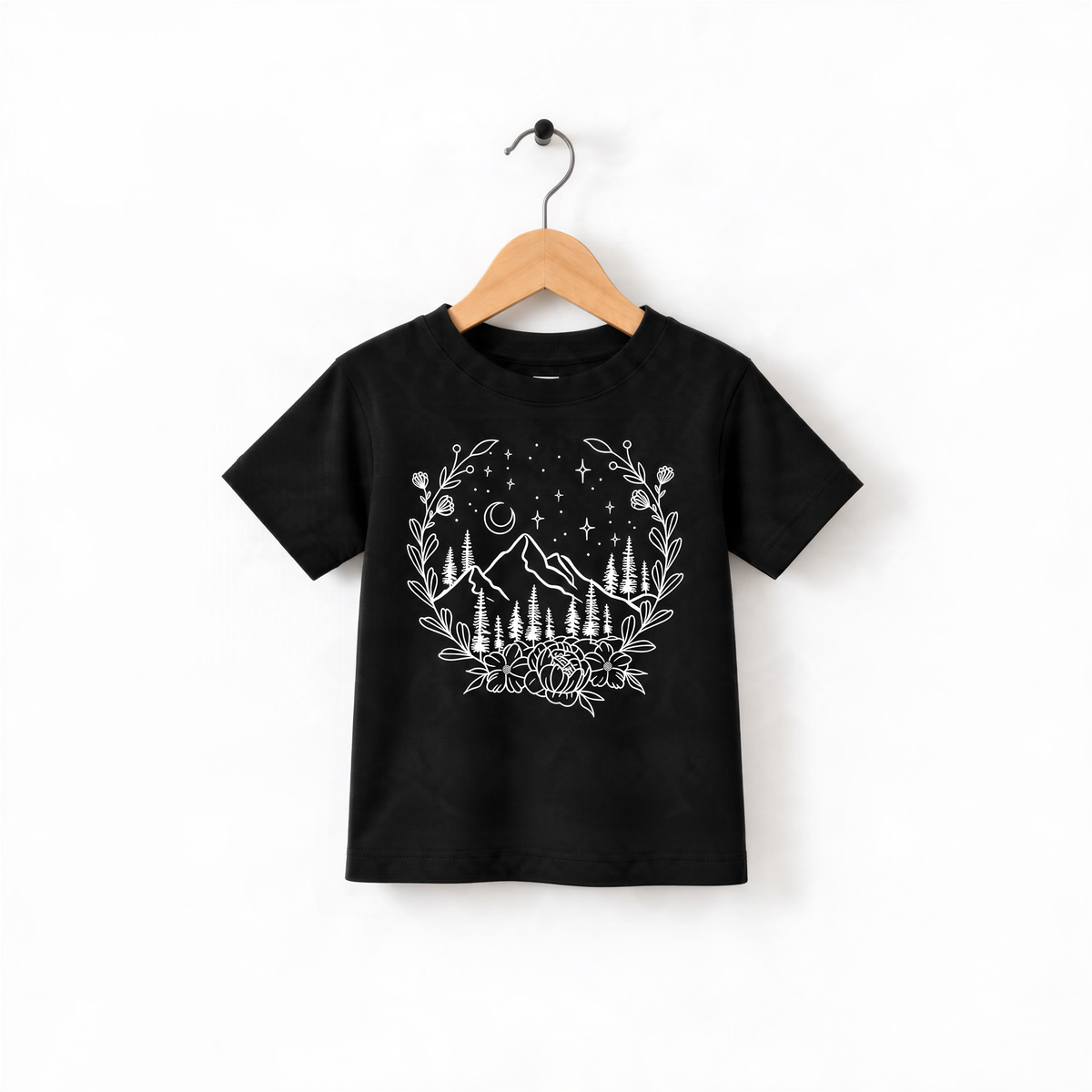 A black t-shirt with a white graphic design depicting a mountain landscape with trees, flowers, and stars.