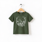 A green t-shirt with a white graphic design depicting a wreath of trees and mountains, along with stars and a crescent moon, hanging on a wooden hanger.