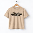 A beige t-shirt with a graphic design depicting a mountain range with trees.