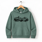 A green hoodie with a graphic of mountains and trees printed on it, hanging on a wooden hanger.