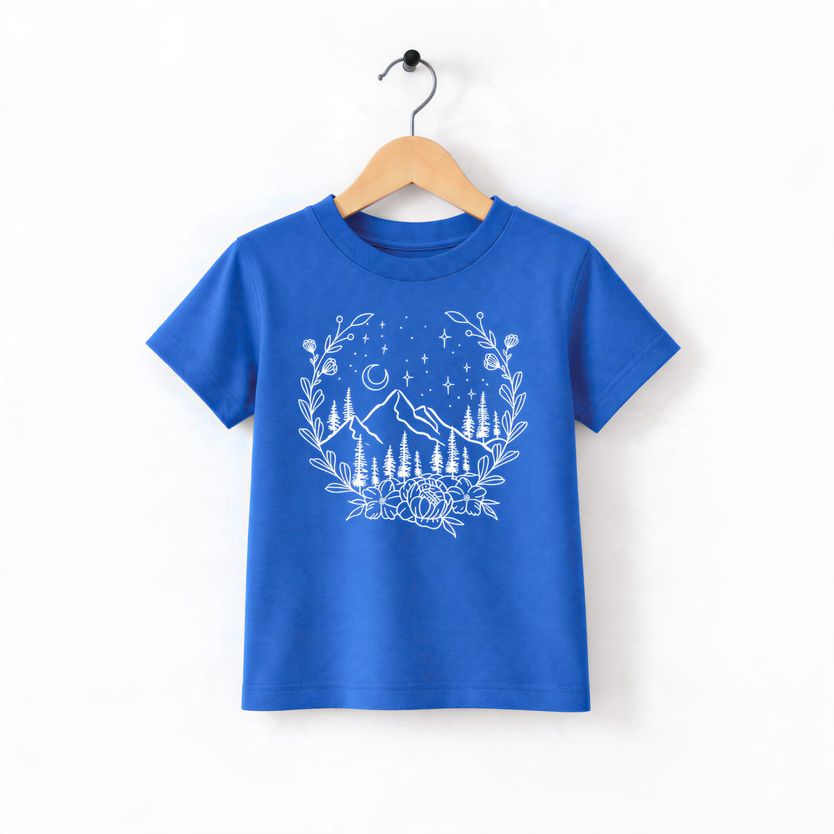 A blue t-shirt with a white graphic design depicting a mountain landscape with trees, flowers, and a night sky.