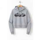 A gray hoodie with a graphic design of mountains and trees printed on it, hanging on a wooden hanger.