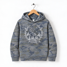 A camouflage hoodie with a white floral design on the front, hanging on a wooden hanger.