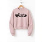 A pink sweatshirt with a graphic design of mountains and trees printed on it, hanging on a wooden hanger.
