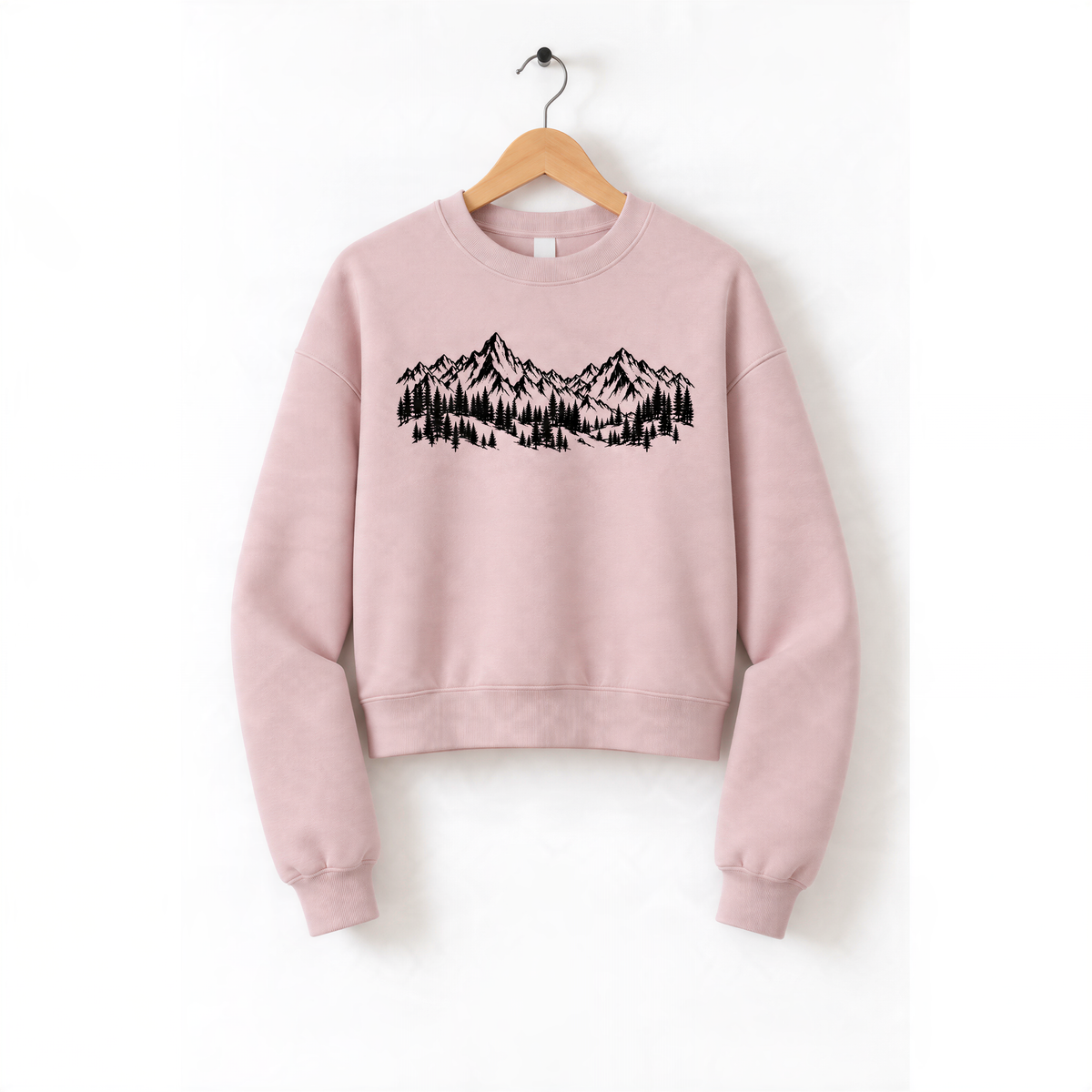 A pink sweatshirt with a graphic design of mountains and trees printed on it, hanging on a wooden hanger.