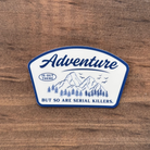 Sticker with 'Adventure' text on a wooden surface