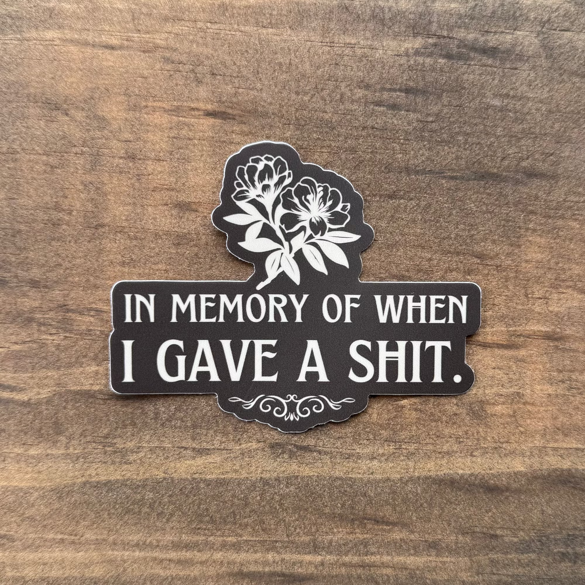 Sticker with text 'In memory of when I gave a shit' on a wooden surface
