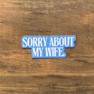Blue sticker with text 'SORRY ABOUT MY WIFE' on a wooden surface