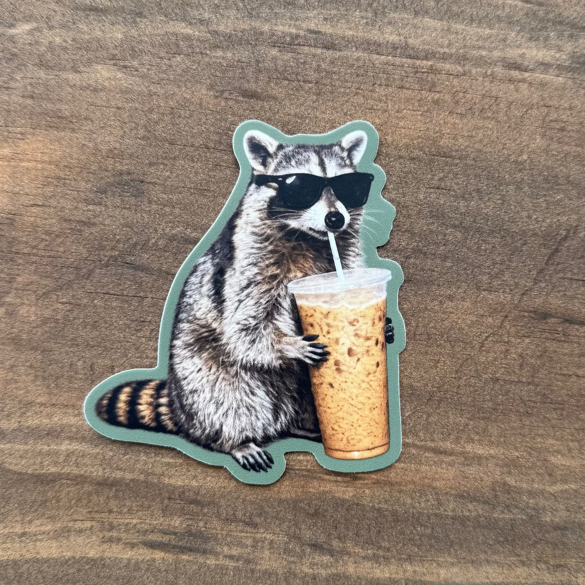 Sticker of a raccoon on a cork with a green border on a wooden surface