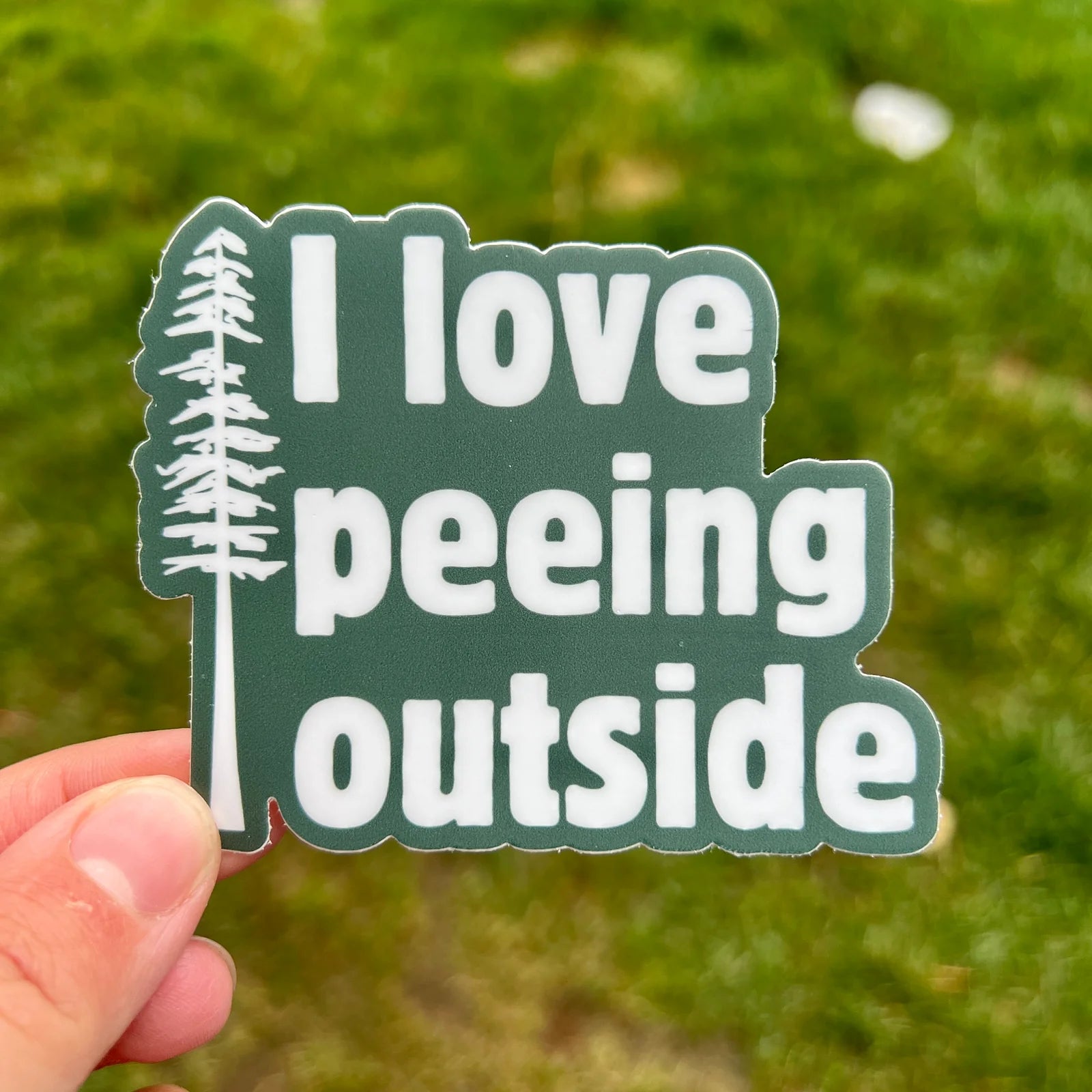 Sticker with 'I love peeing outside' text held against a grassy background