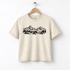 A beige t-shirt with a graphic design depicting a mountain range with pine trees.