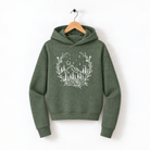 A green hoodie with a white floral design on the front, hanging on a wooden hanger against a white background.