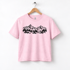 A pink t-shirt with a graphic design of mountains and trees printed on it.