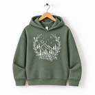 A green hoodie with a white graphic design depicting a mountain landscape with trees, flowers, and stars on a wooden hanger.