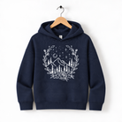 A navy blue hoodie with a white graphic design depicting a mountain landscape with trees, flowers, and stars on a wooden hanger.