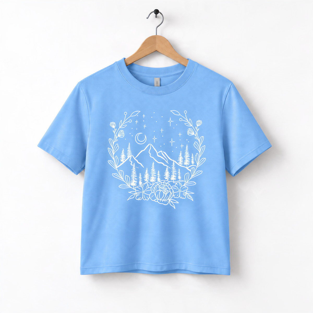 A light blue t-shirt with a white graphic design depicting a mountain landscape with trees, flowers, and stars.