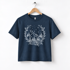A navy blue t-shirt with a white graphic design depicting a mountain landscape with trees, flowers, and a starry night sky.