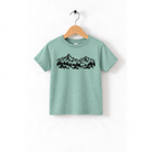 A light green t-shirt with a graphic design of mountains and trees printed on it, hanging on a wooden hanger.