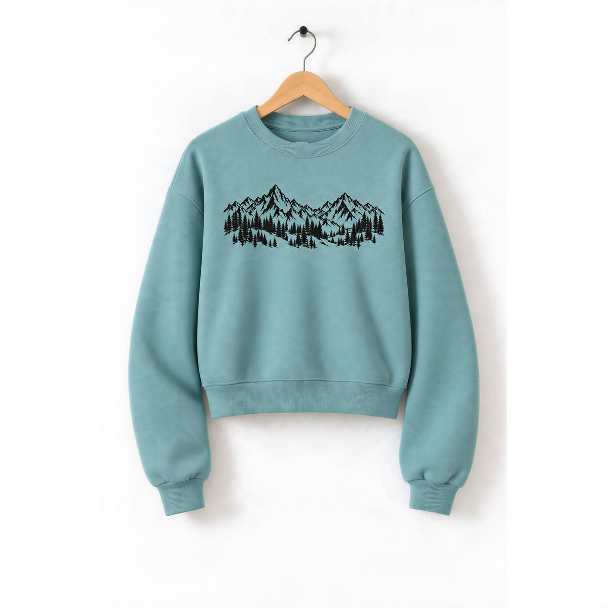 A light blue sweatshirt with a graphic of mountains and trees printed on it, hanging on a wooden hanger.