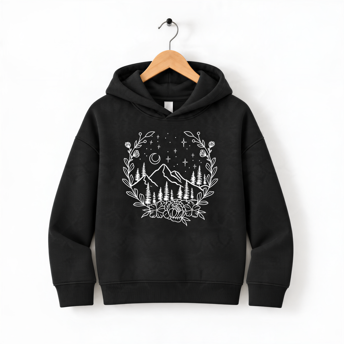 A black hoodie with a white graphic design depicting a wreath of trees and mountains, along with stars and a crescent moon, hanging on a wooden hanger.