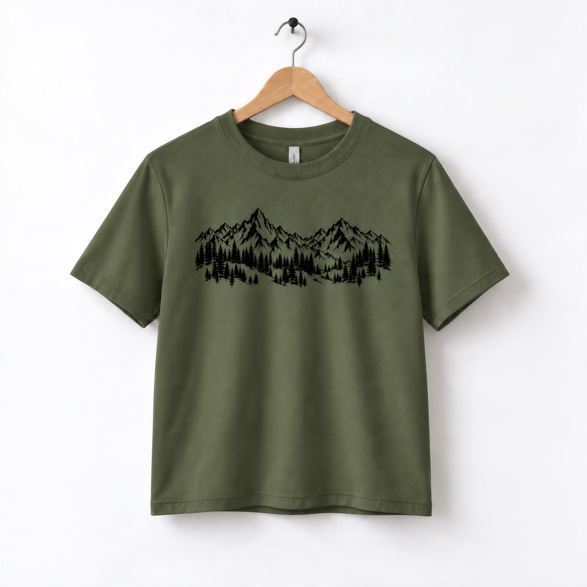 A green t-shirt with a graphic design of mountains and trees printed on it, hanging on a wooden hanger.