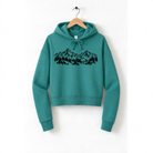 A teal hoodie with a mountain landscape design printed on it, hanging on a wooden hanger.